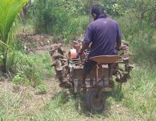 A father is on a small brown tractor which is operated by pedalling it down the hill. 