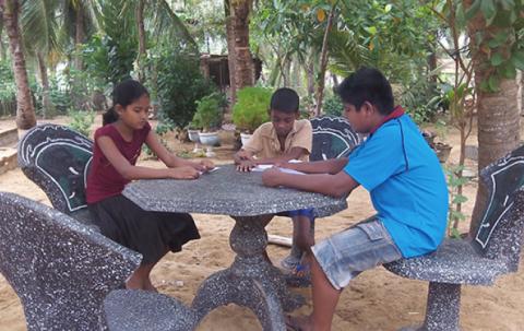 A girl and two boys are sitting around a black stone table with white spots.