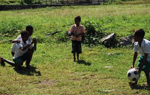 A boy from Timor Leste is filming another boy kicking the soccer ball.